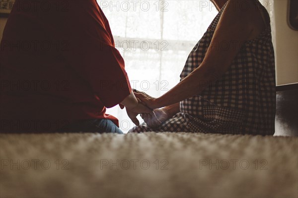 Older woman holding hand of daughter on bed