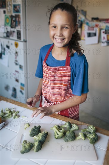 Smiling girl chopping broccoli in kitchen