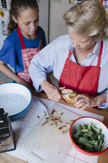 Grandmother and granddaughter peeling potato in kitchen