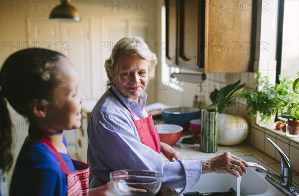 Grandmother and granddaughter washing bowl in kitchen sink