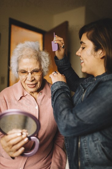 Granddaughter combing hair of grandmother holding mirror