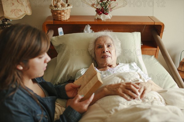 Granddaughter reading to grandmother in bed