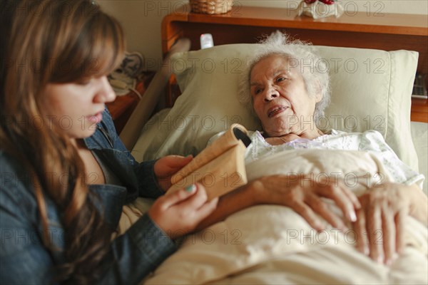 Granddaughter reading to grandmother in bed