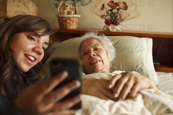 Grandmother and granddaughter taking selfie with cell phone in bed