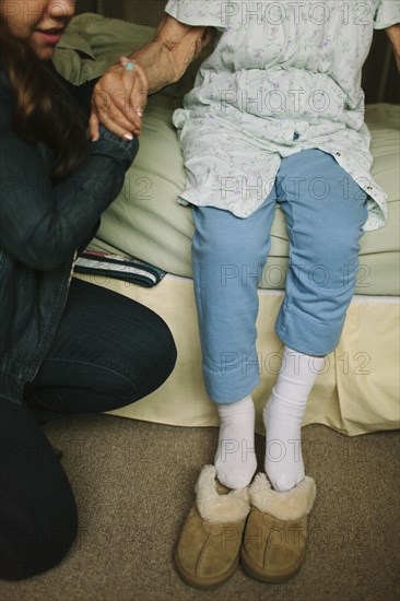 Granddaughter helping grandmother out of bed into slippers