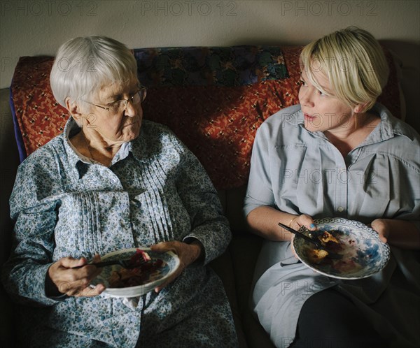 Older woman and granddaughter eating on sofa