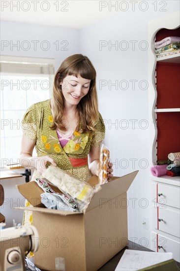 Mixed race dressmaker unpacking box at sewing table