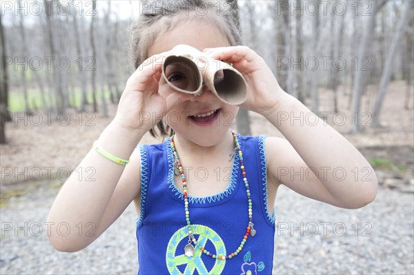 Caucasian girl playing with cardboard tubes in forest