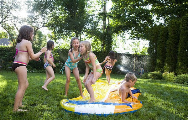 Children playing on water slide in backyard