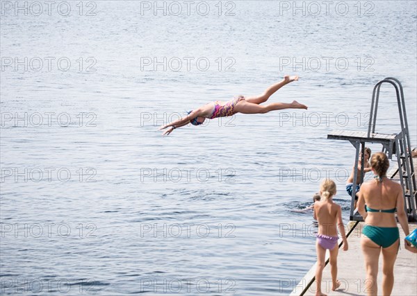 Caucasian girl jumping from diving board into lake