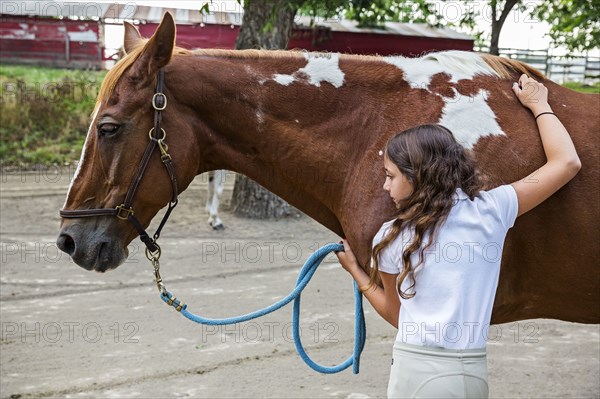 Teenage girl hugging horse on ranch