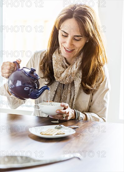 Caucasian woman pouring cup of tea at table