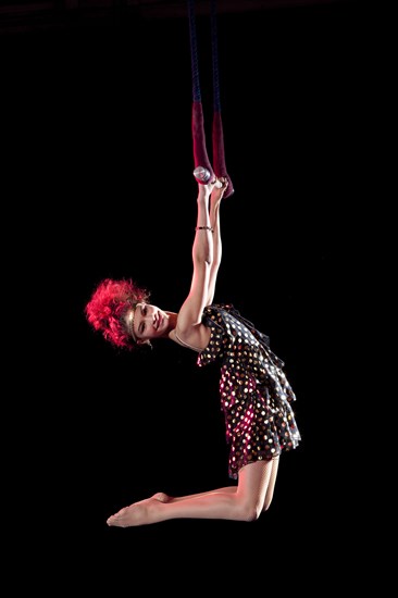 Mixed race acrobat hanging from trapeze