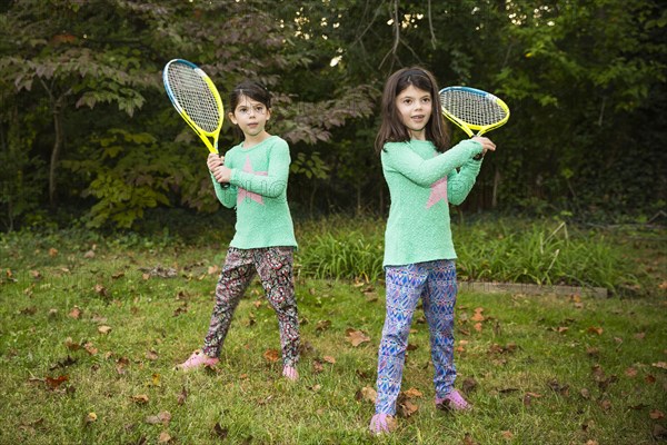 Twin sisters playing tennis in grass