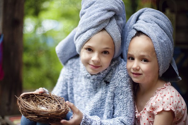 Caucasian sisters in hair towels holding bird nest