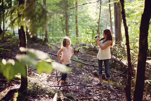 Caucasian girl photographing sister in forest