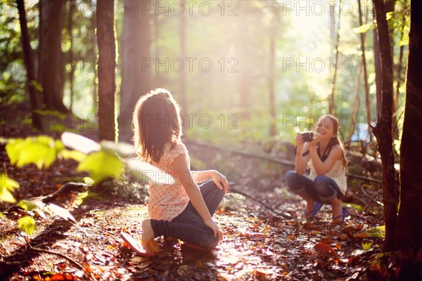 Caucasian girl photographing sister in forest