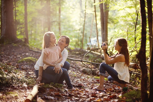 Caucasian girl photographing mother and sister in forest