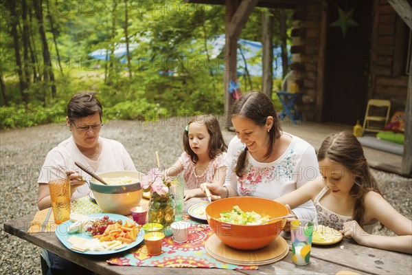 Three generations of Caucasian women eating outside cabin