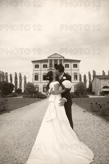 Caucasian bride and groom kissing on gravel path