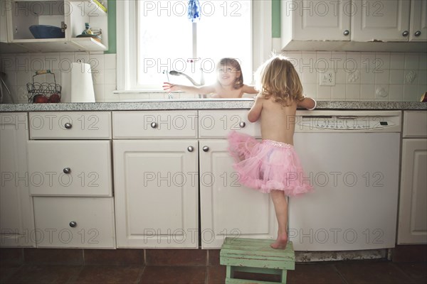 Sisters playing at kitchen sink