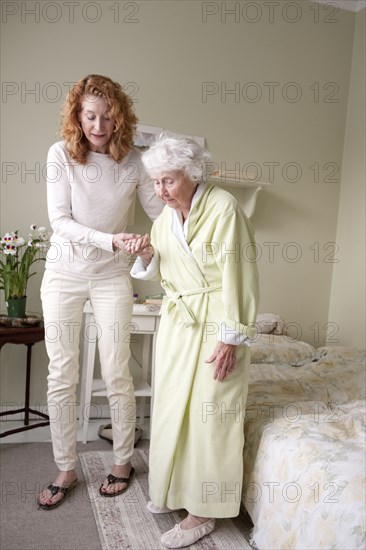 Woman helping mother walk in bedroom