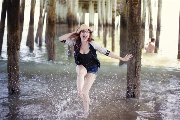 Caucasian woman splashing in ocean under boardwalk