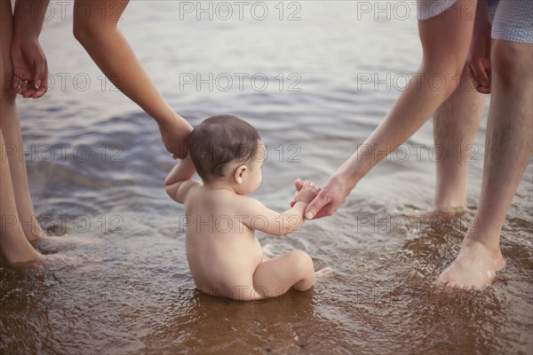 Parents helping baby sit in lake