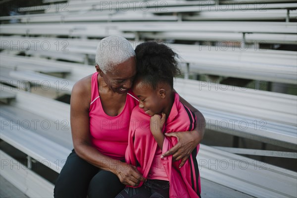 Grandmother wrapping sweater around granddaughter on bleachers