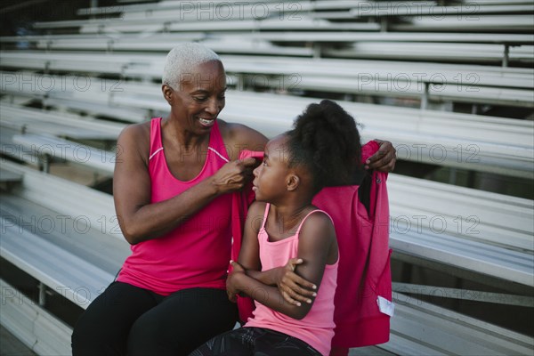 Grandmother wrapping sweater around granddaughter on bleachers