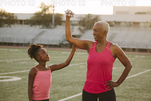 Girl squeezing biceps of grandmother on football field