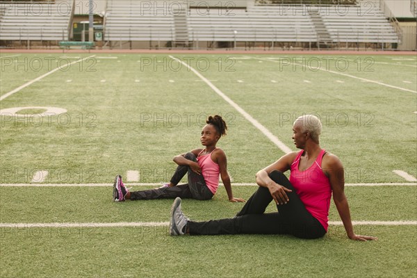 Grandmother and granddaughter stretching on football field