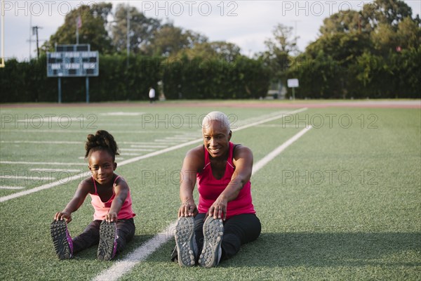 Grandmother and granddaughter stretching on football field