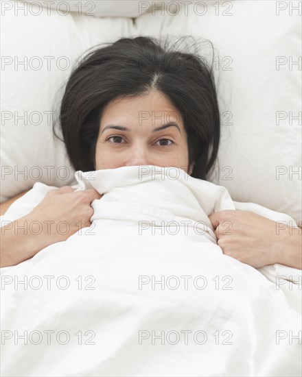 Hispanic woman in bed covering her face