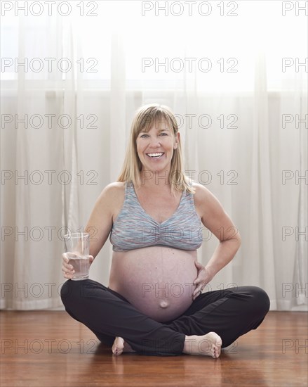 Pregnant Caucasian woman sitting on floor drinking water