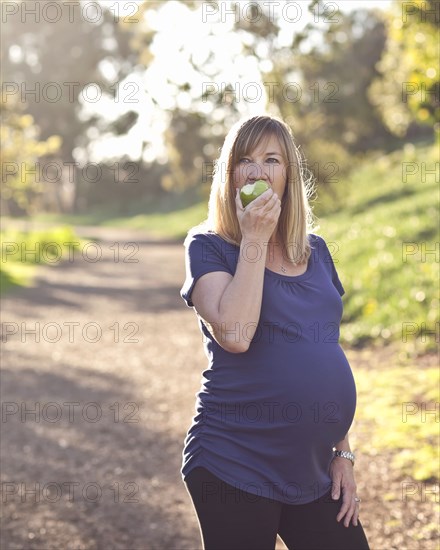 Pregnant Caucasian woman eating apple outdoors