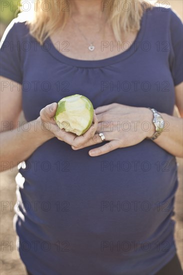 Pregnant Caucasian woman eating apple outdoors