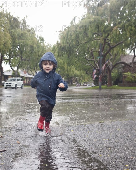 Caucasian boy splashing in rain puddle