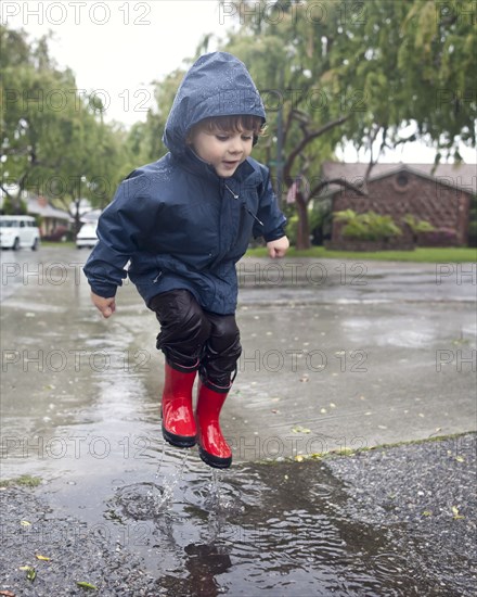 Caucasian boy jumping in rain puddle