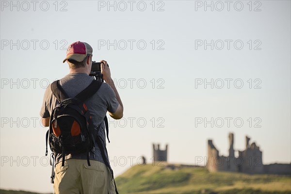 Caucasian tourist photographing Dunstanburgh castle