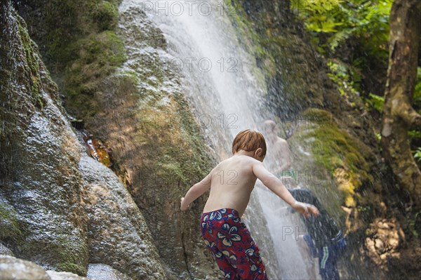 Caucasian boy playing in jungle waterfall