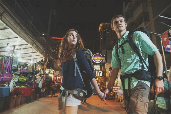 Caucasian tourists holding hands in market at night