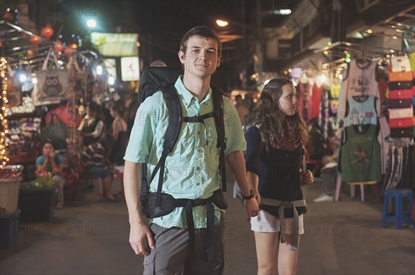 Caucasian tourists holding hands in market at night