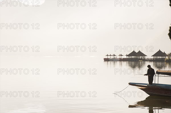 Fisherman standing in boat on still remote lake