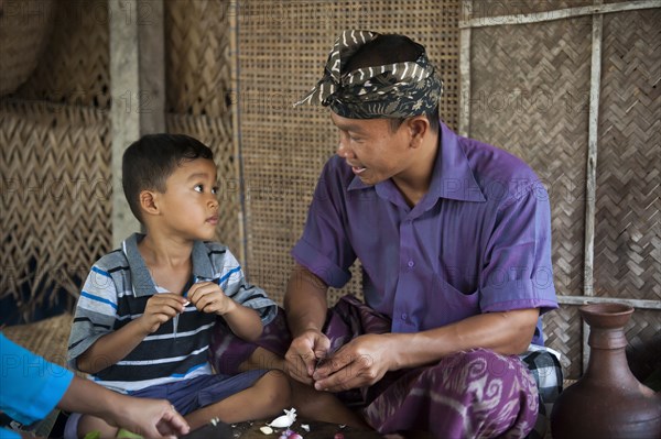 Asian father and son peeling garlic in living room