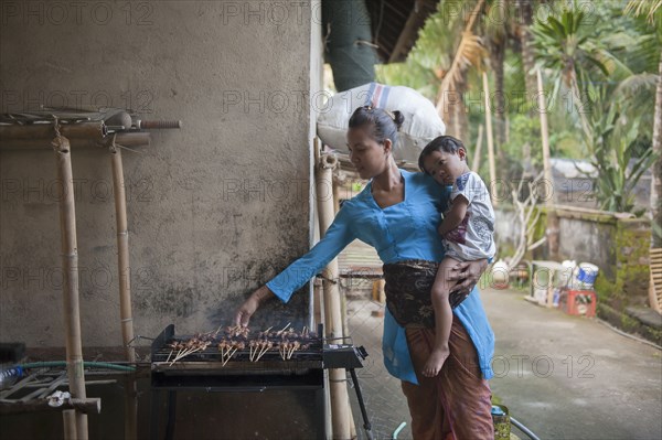 Asian mother and son cooking on grill outdoors