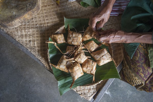 Asian man knotting woven packages on floor