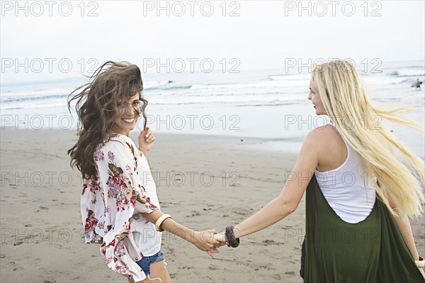 Caucasian women holding hands on beach