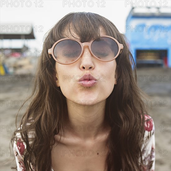 Caucasian woman in sunglasses puckering to kiss at beach