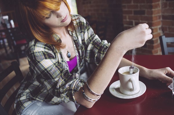 Caucasian woman sprinkling sugar in coffee